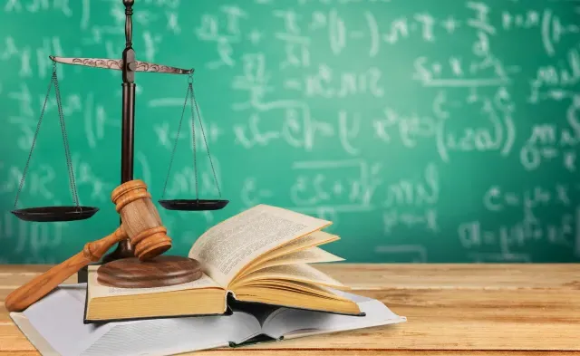 Gavel on books on a desk with scales and chalkboard in background